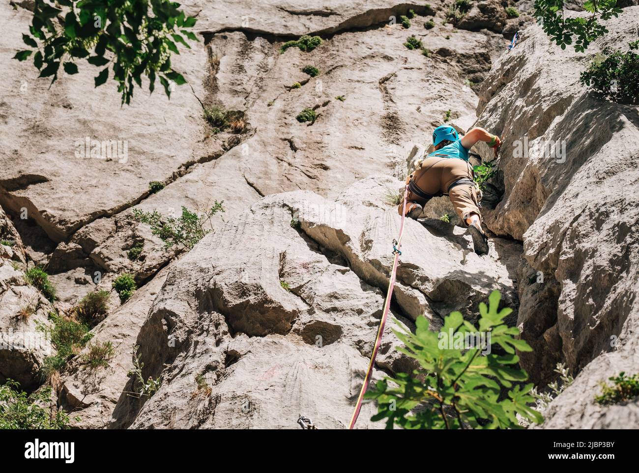Athletische Frau in Schutzhelm und Schuhen auf Felswand führen Klettern mit Seil und Klettergurt im Nationalpark Paklenica, Kroatien. Ac Stockfoto