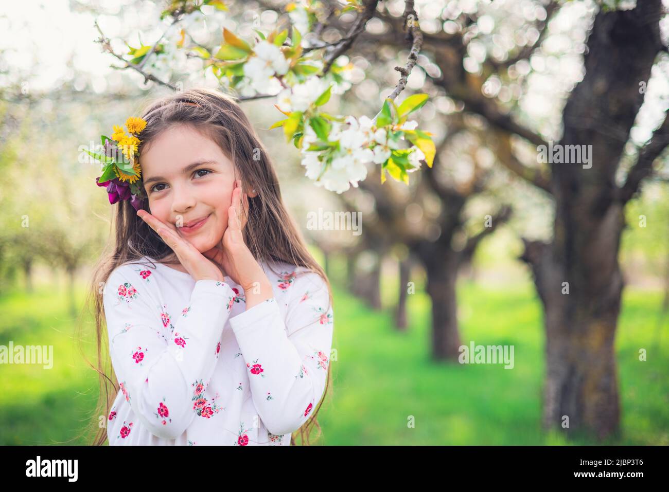 Glückliches schönes Mädchen genießen blühende Frühlingsbäume in Apfelgarten. Bulgarische Frau in Folklore-Kleid auf dem Feld. Stockfoto