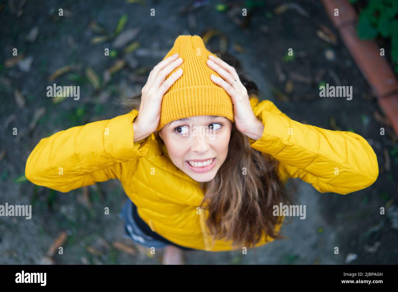 Frau mit gelbem Hut und Mantel, mit Händen über dem Kopf und einem oops-Ausdruck Stockfoto