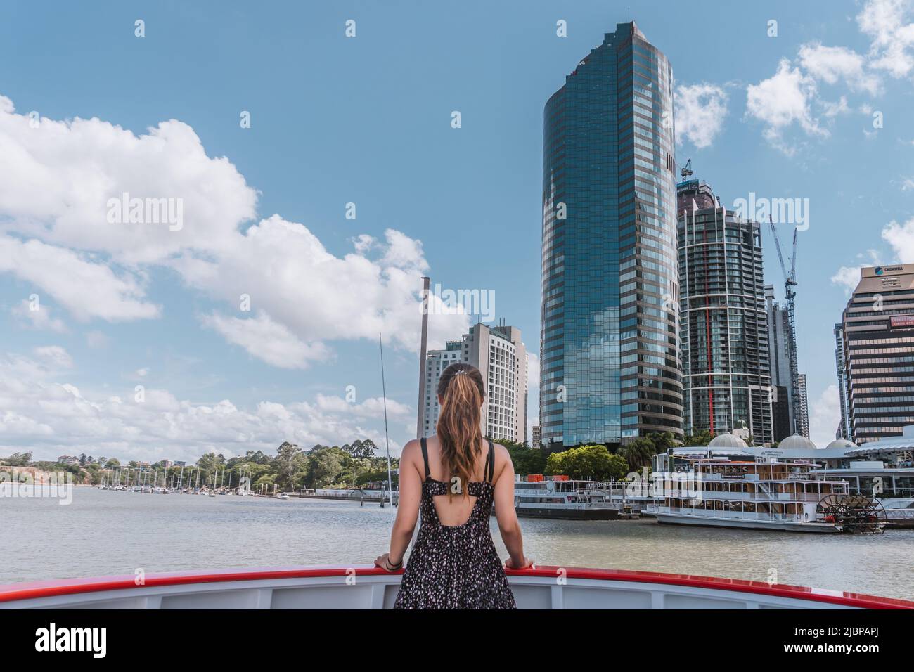 Frau, die auf der Fähre von Brisbane steht und hohen Gebäuden des Geschäftszentrums von Brisbane gegenübersteht. Stockfoto