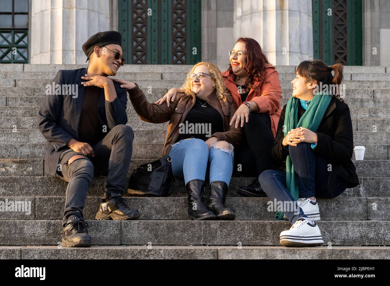 Multiethnische Gruppe von Freunden, die auf einigen Treppen sitzen und sich unterhalten und lachen Stockfoto