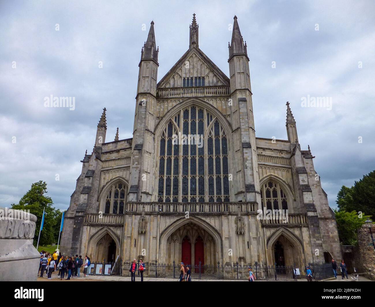 In Winchester, Hampshire, England, Großbritannien, erhebt sich die mittelalterliche Winchester Cathedral unter einem bewölkten Himmel über Touristen. Stockfoto