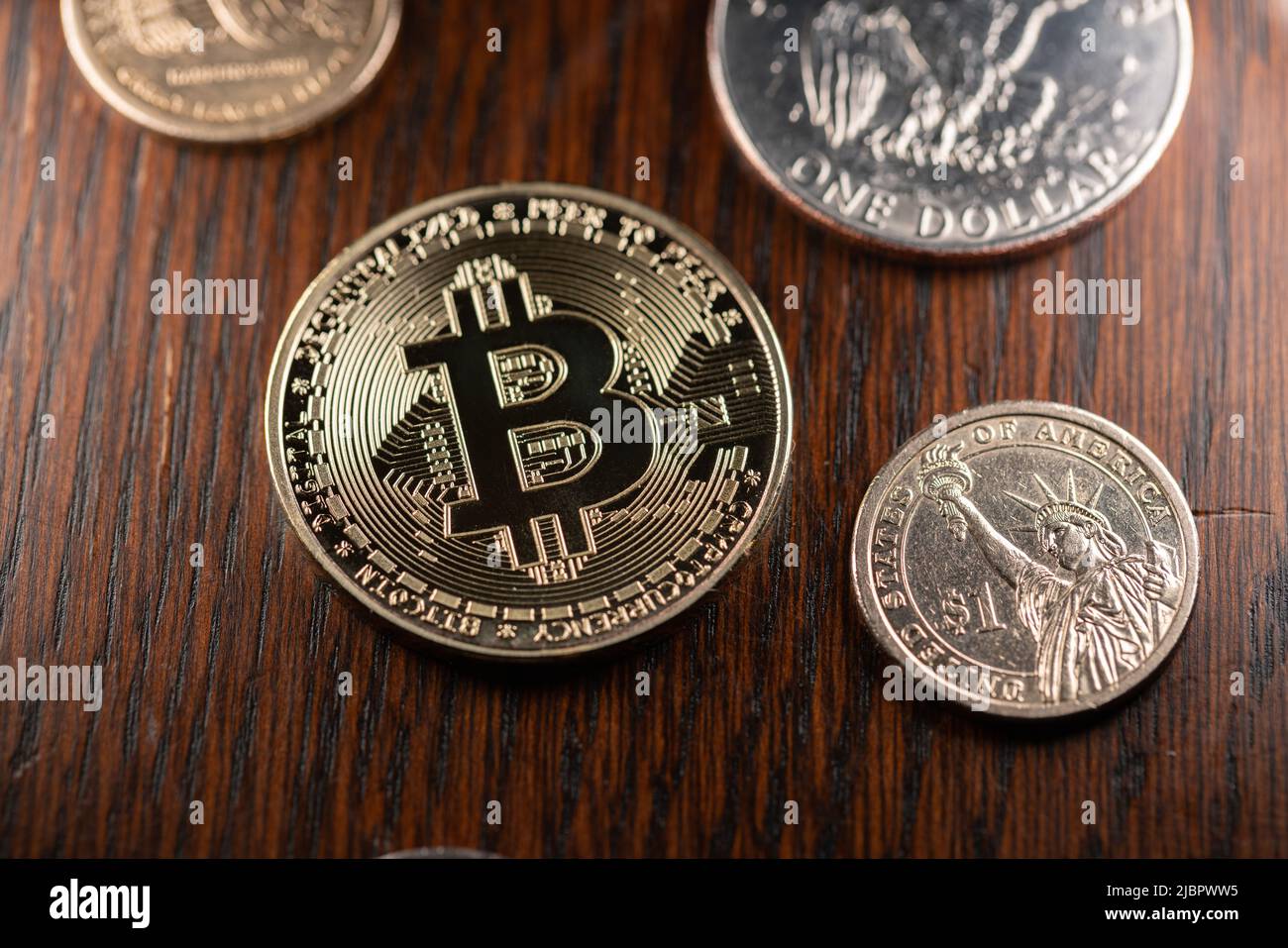 Bitcoin- und 1-Dollar-Münzen auf dunklem Holz-Hintergrund. Gold BTC Münze neben 1 Dollar Münze. US-Dollar-Währung im Vergleich zu Kryptowährung. Stockfoto