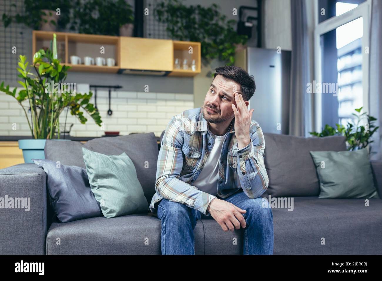 Der Kranke sitzt allein zu Hause auf der Couch, hat starke Kopfschmerzen Stockfoto