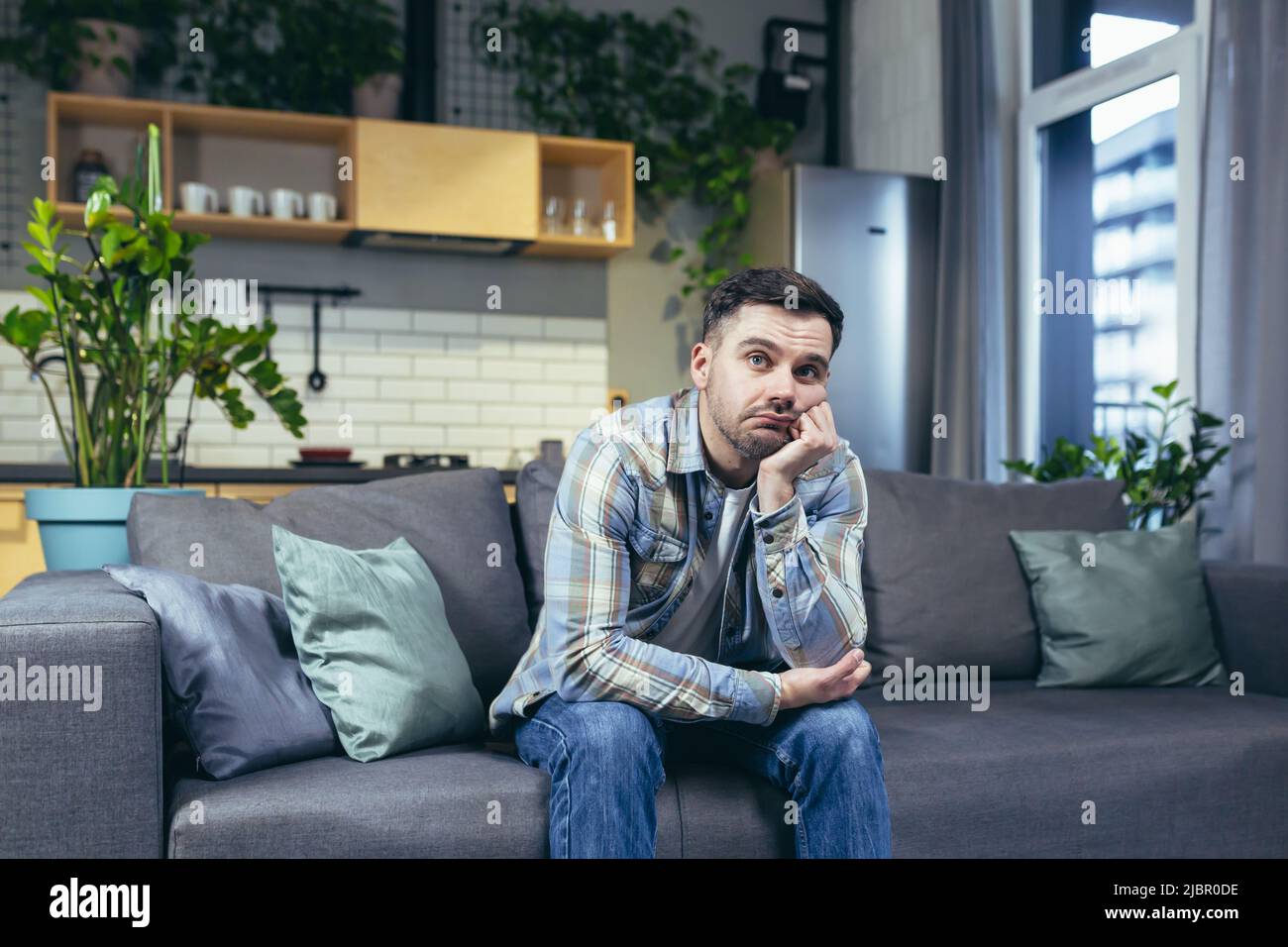 Trauriger und nachdenklicher Mann, der zu Hause auf der Couch sitzt Stockfoto
