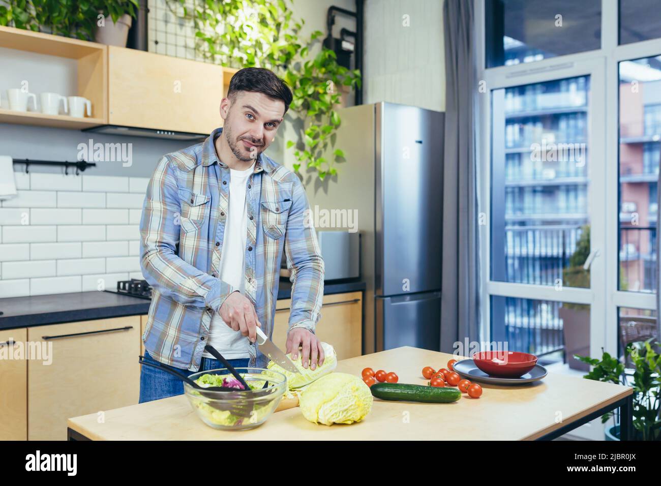 Der Mann bereitet zu Hause gesunde und gesunde Lebensmittel zu, schneidet Gemüse für Salat in der Küche Stockfoto