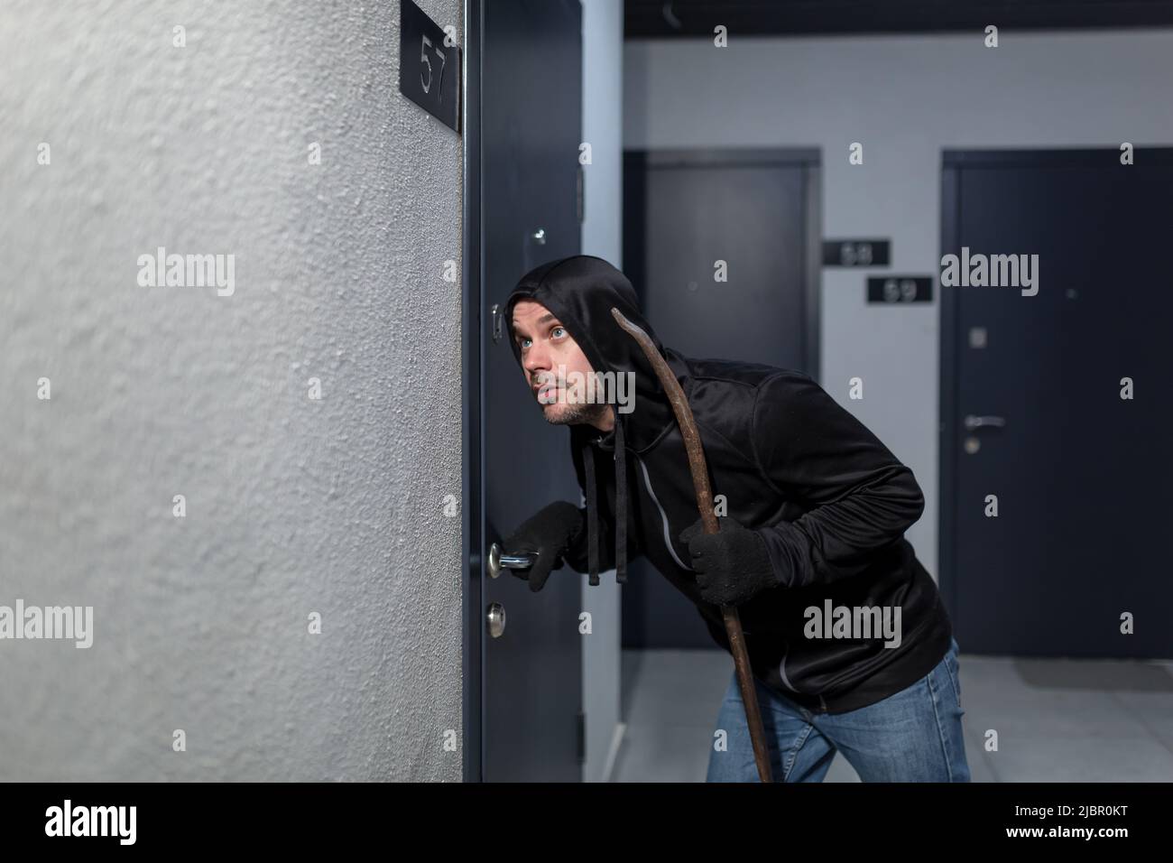 Der Räuber versucht, das Türschloss in der Wohnung zu brechen, in Schwarz gekleidet Stockfoto