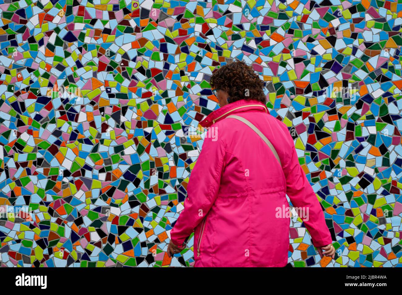 Frau in roter Jacke passiert das farbenfrohe Keramik-Mosaik-Kunstwerk Rivertime von Hermann-Josef Kuhna in Düsseldorf, Nordrhein-Westfalen, Deutschland 24.5.22 Stockfoto