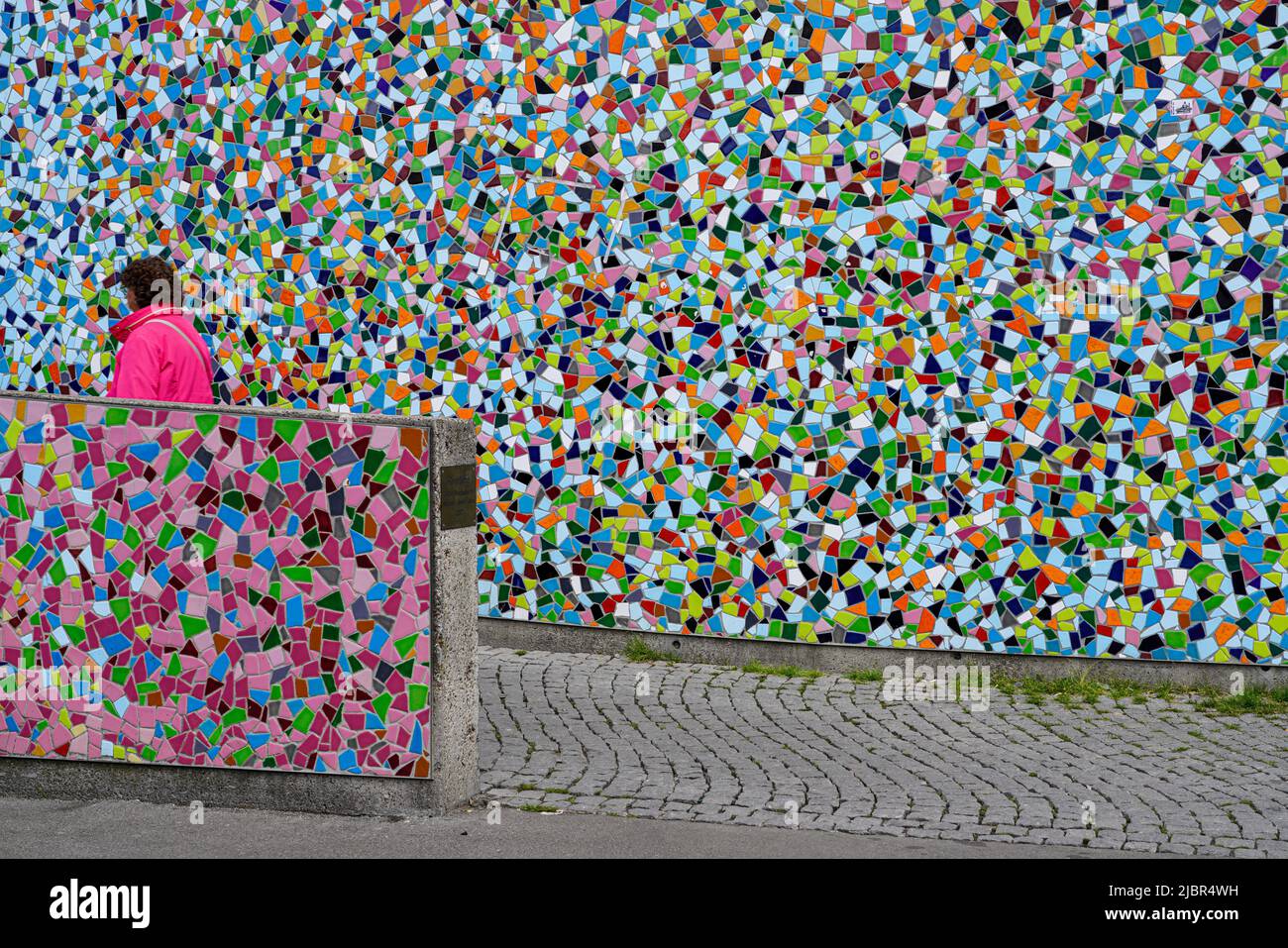 Frau in roter Jacke passiert das farbenfrohe Keramik-Mosaik-Kunstwerk Rivertime von Hermann-Josef Kuhna in Düsseldorf, Nordrhein-Westfalen, Deutschland 24.5.22 Stockfoto