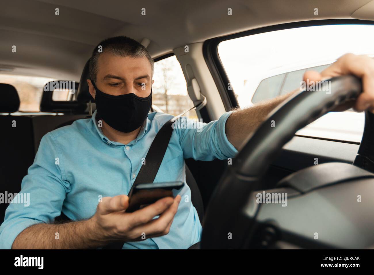 Mann, Der Auto Mit Smartphone Trägt Gesichtsmaske Im Auto Stockfoto