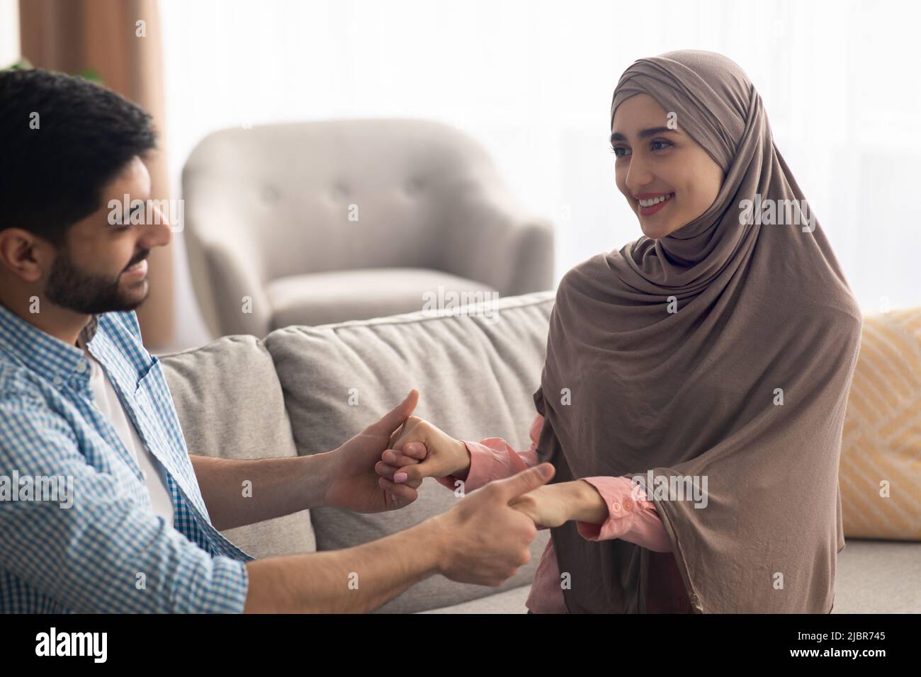 Liebendes Muslimisches Paar, Das Hände Auf Dem Sofa Zu Hause Hält Stockfoto