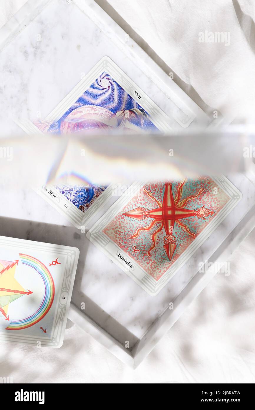 Thoth Astrology Tarot Kartendeck auf weißem Marmorhintergrund mit Regenbogenlicht-Prisma und verträumten floralen Schatten Stockfoto