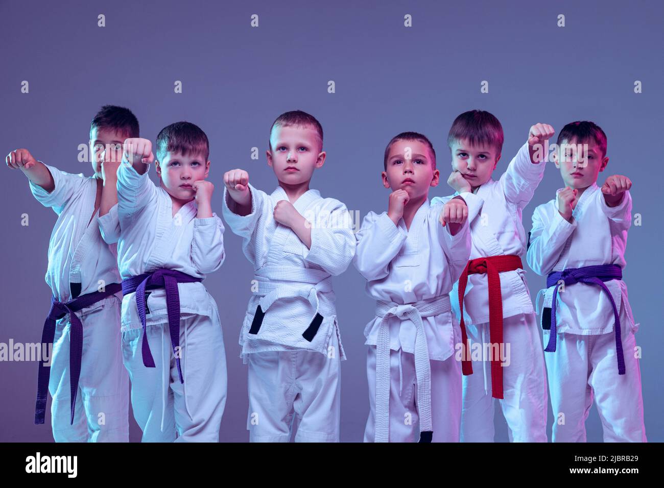 Gruppe von Kindern, verschiedenen Jungen, Taekwondo Athleten in weißen doboks in Aktion isoliert auf lila Farbe Hintergrund. Konzept des Sports, Kampfkunst Stockfoto