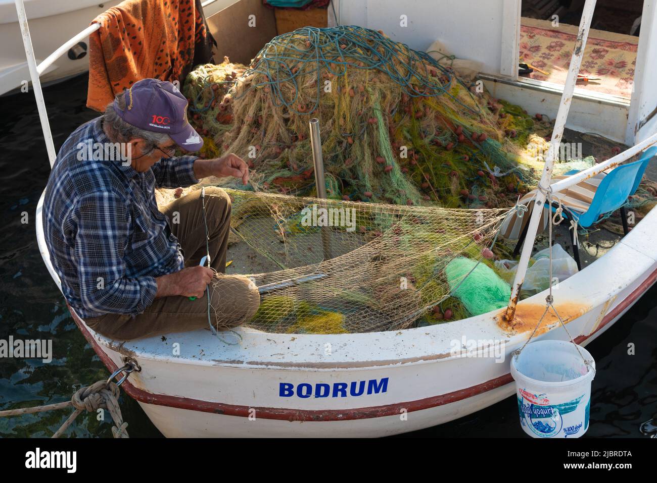 Bodrum, Mugla, Türkei. April 23. 2022 Ein Fischer, der Netze auf seinem Boot ausbessern im Hafen von Bodrum ist die ägäische Küstenlage in der Türkei ein beliebtes Reiseziel Stockfoto