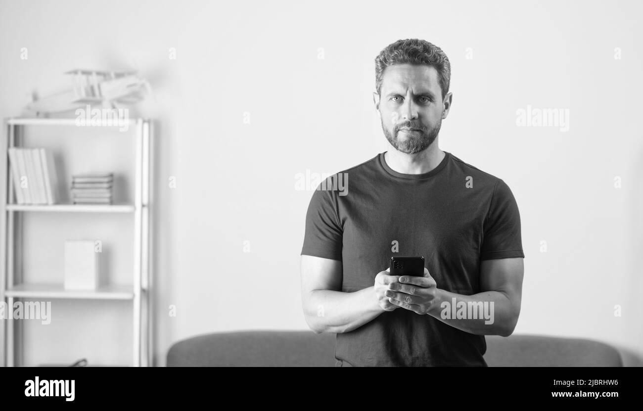 Bärtiger Kerl in rotem T-Shirt, der auf dem Handy chattet, im Internet surft Stockfoto