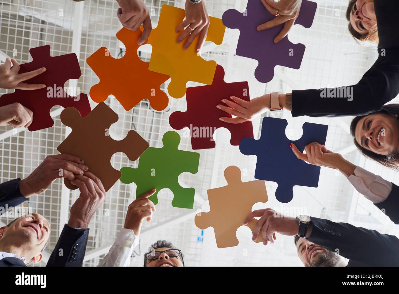Fröhliche männliche und weibliche Büroangestellte stellten farbige Puzzleteile zusammen, wenn sie sich im Büro treffen. Stockfoto
