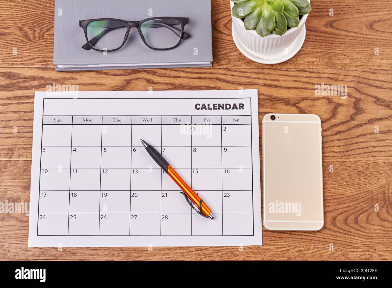 Draufsicht flacher Lay-Kalender mit Smartphone und Stift. Buch mit Gläsern und Topf mit Pflanze. Stockfoto