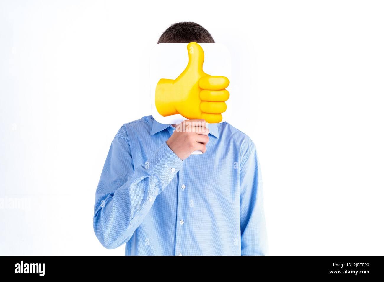 Social Media, Blogging und People-Konzept - Teenager-Junge in blauem Hemd mit Daumen nach oben Emoticon auf weißem Hintergrund. Das Gesicht ist geschlossen. Türkei, Ist Stockfoto