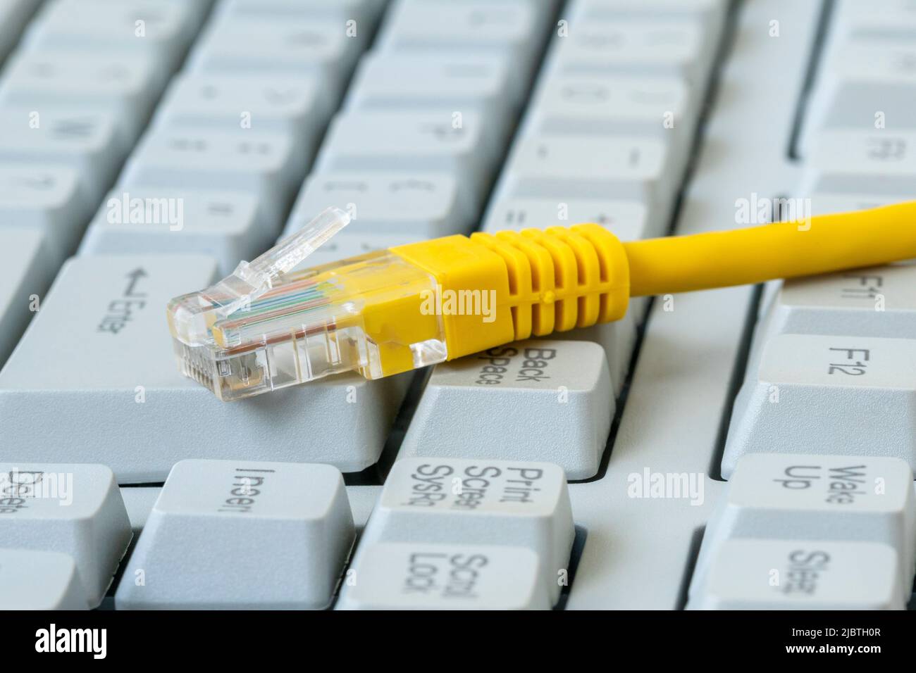 Gelber Internetschalter auf der alten Computertastatur mit großen Tasten. Internetkabel, RJ-45-Stecker an der Computertastatur. Stockfoto