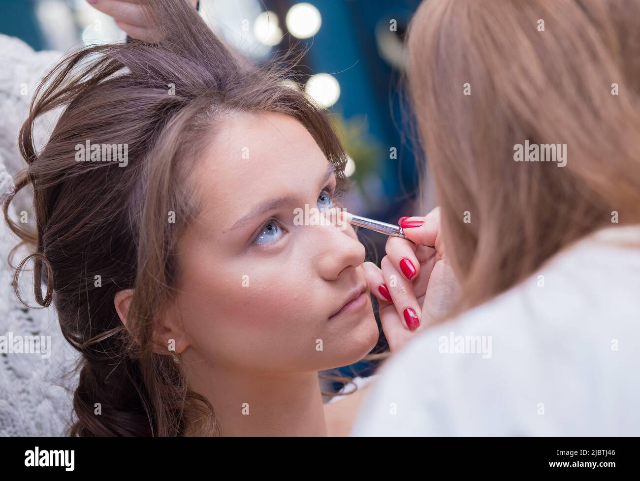 Ein professioneller Make-up-Künstler malt das Auge eines Kunden mit einem Pinsel. Weibliche Meisterin macht einer jungen Frau Make-up. Geschäftskonzept - Schönheitssalon, Gesichtshautpflege, Kosmetik. Stockfoto