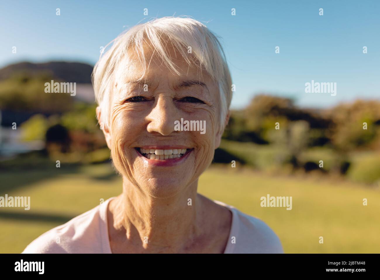 Nahaufnahme des Porträts einer fröhlichen asiatischen älteren Frau mit kurzen Haaren vor dem klaren blauen Himmel im Hof Stockfoto