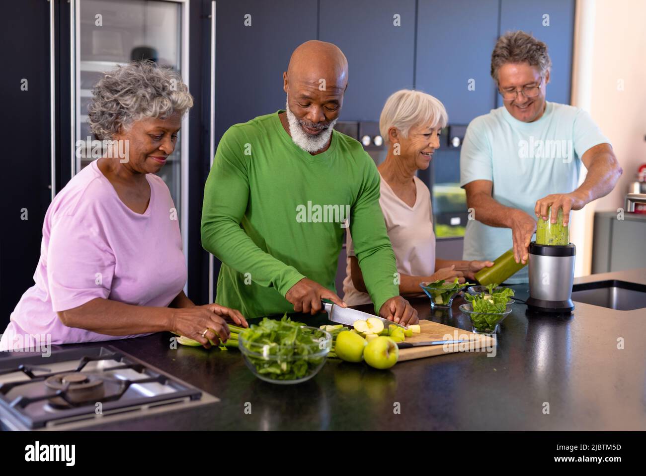 Freunde von Senioren aus verschiedenen Rassen hacken Obst, Gemüse und mischen Smoothie auf der Küchentheke Stockfoto