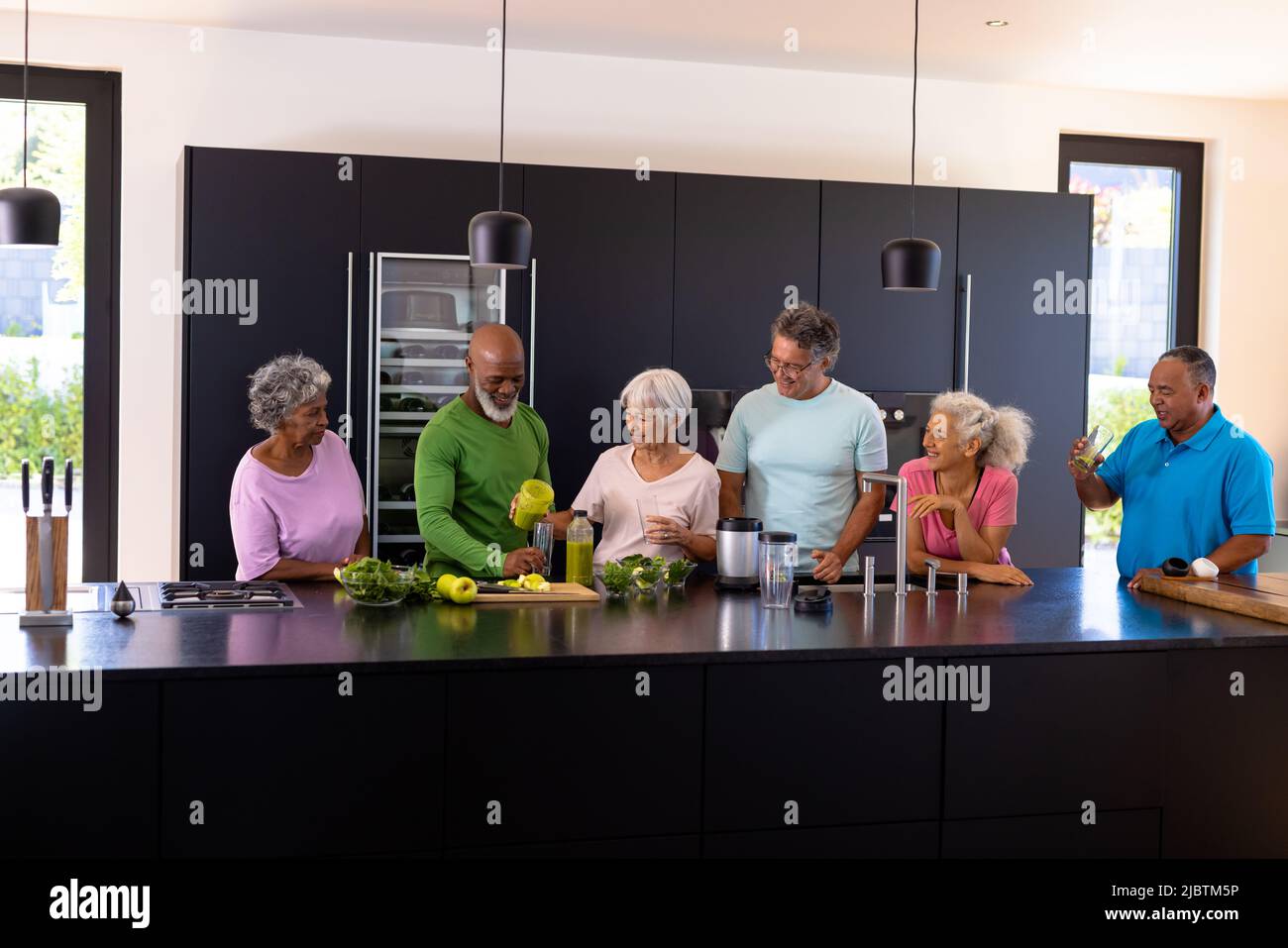 Multirassische Senioren sprechen und bereiten Gemüse und Obst Smoothie in der Küche zu Stockfoto