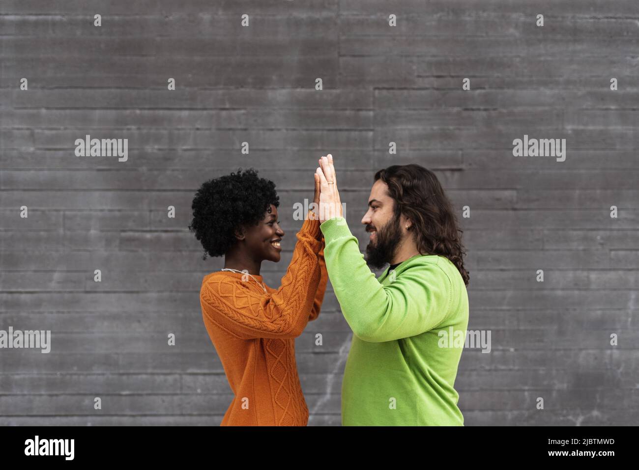 Glückliches interrassisches Paar, das sich anschaut und sich die Hände anschließt, während es im Freien steht. Stockfoto