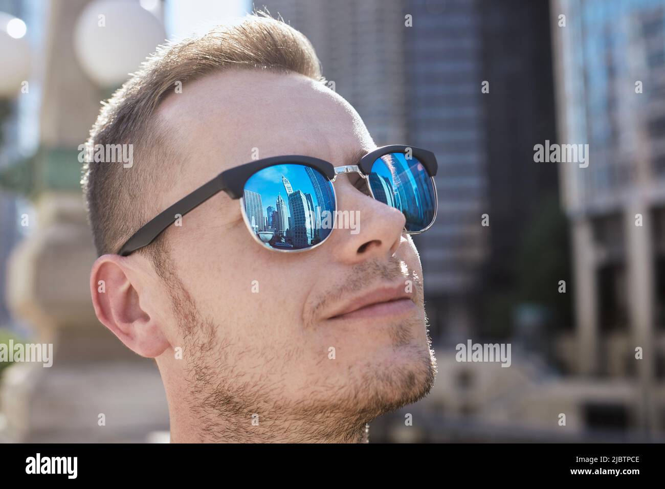 Spiegelung von Wolkenkratzern in Sonnenbrillen eines jungen Mannes. Touristen bewundern historische Gebäude in der Stadt. Themen des Tourismus und Augenschutz. Stockfoto