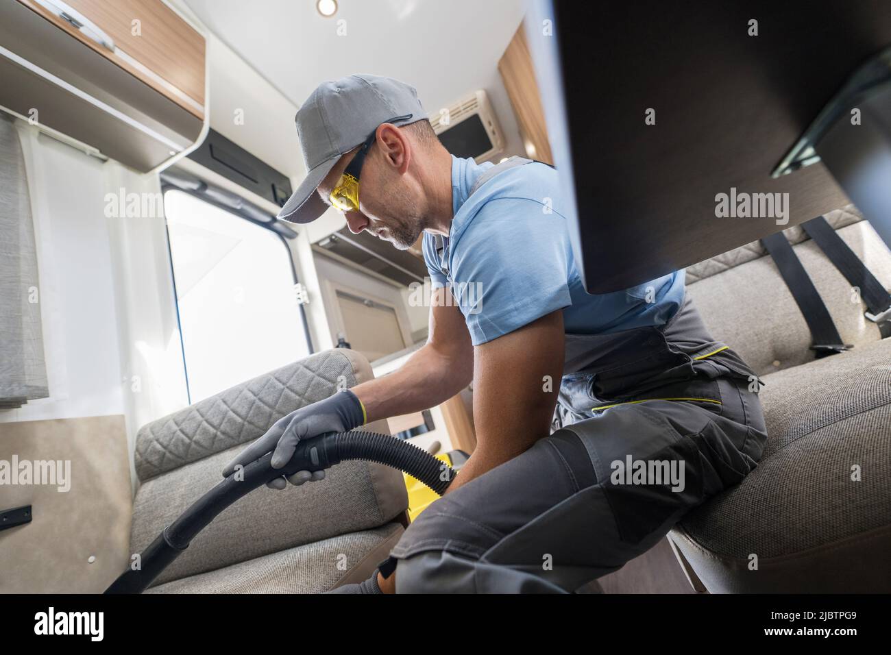 Männlicher Arbeiter in seinem 40s Reinigung der Sofa-Bett-Couch in einem Wohnmobil Fahrzeug mit einem Staubsauger. Pflege und Pflege eines modernen und komfortablen Campers Stockfoto