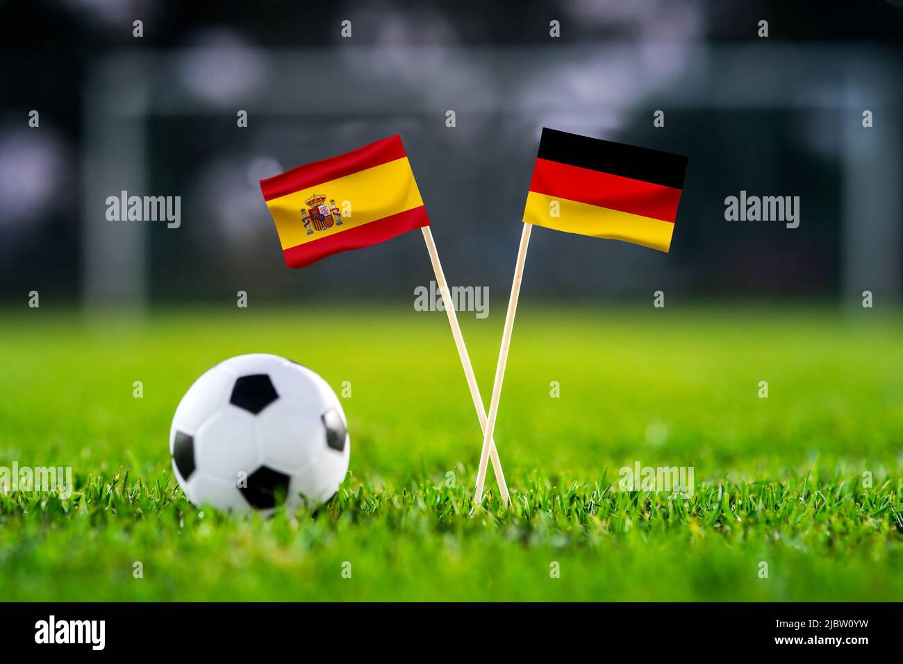 Spanien vs. Deutschland, Al Bayt, Fußballspiel-Tapete, Handgefertigte Nationalflaggen und Fußball auf grünem Gras. Fußballstadion im Hintergrund. Schwarz ed Stockfoto