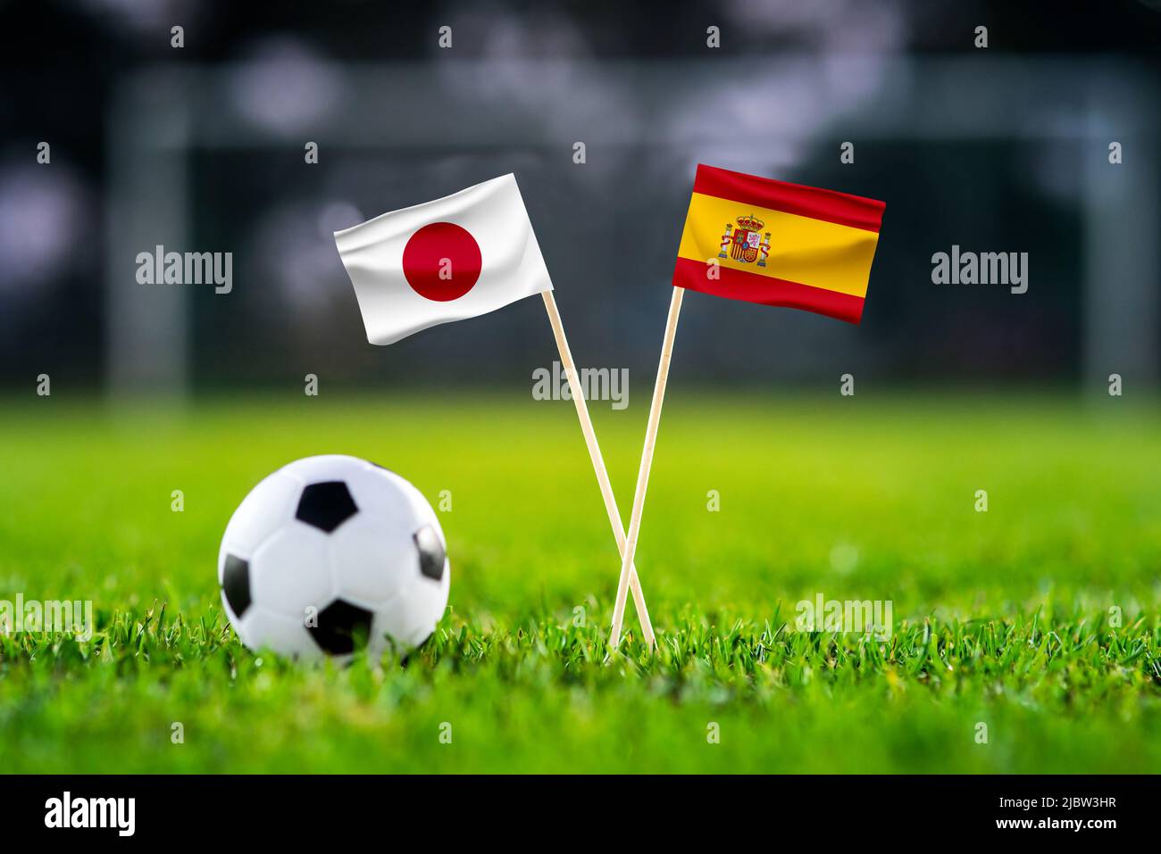 Japan vs. Spanien, Khalifa-Stadion, Fußballspiel-Tapete, handgefertigte Nationalflaggen und Fußball auf grünem Gras. Fußballstadion im Hintergrund. Bl Stockfoto