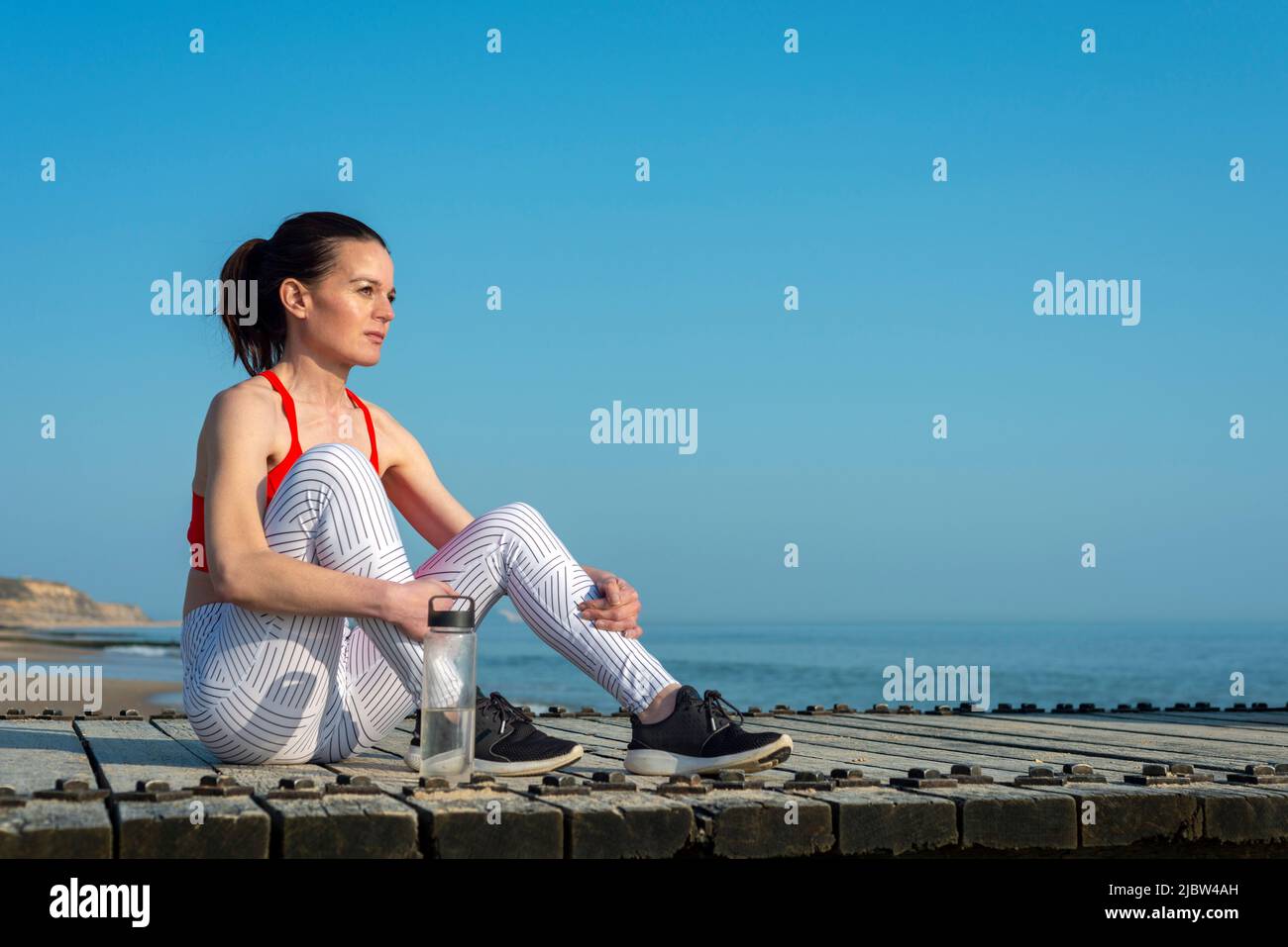 Fit, sportlich Frau sitzen und entspannen nach dem Sport am Meer mit einer Flasche Wasser. Stockfoto