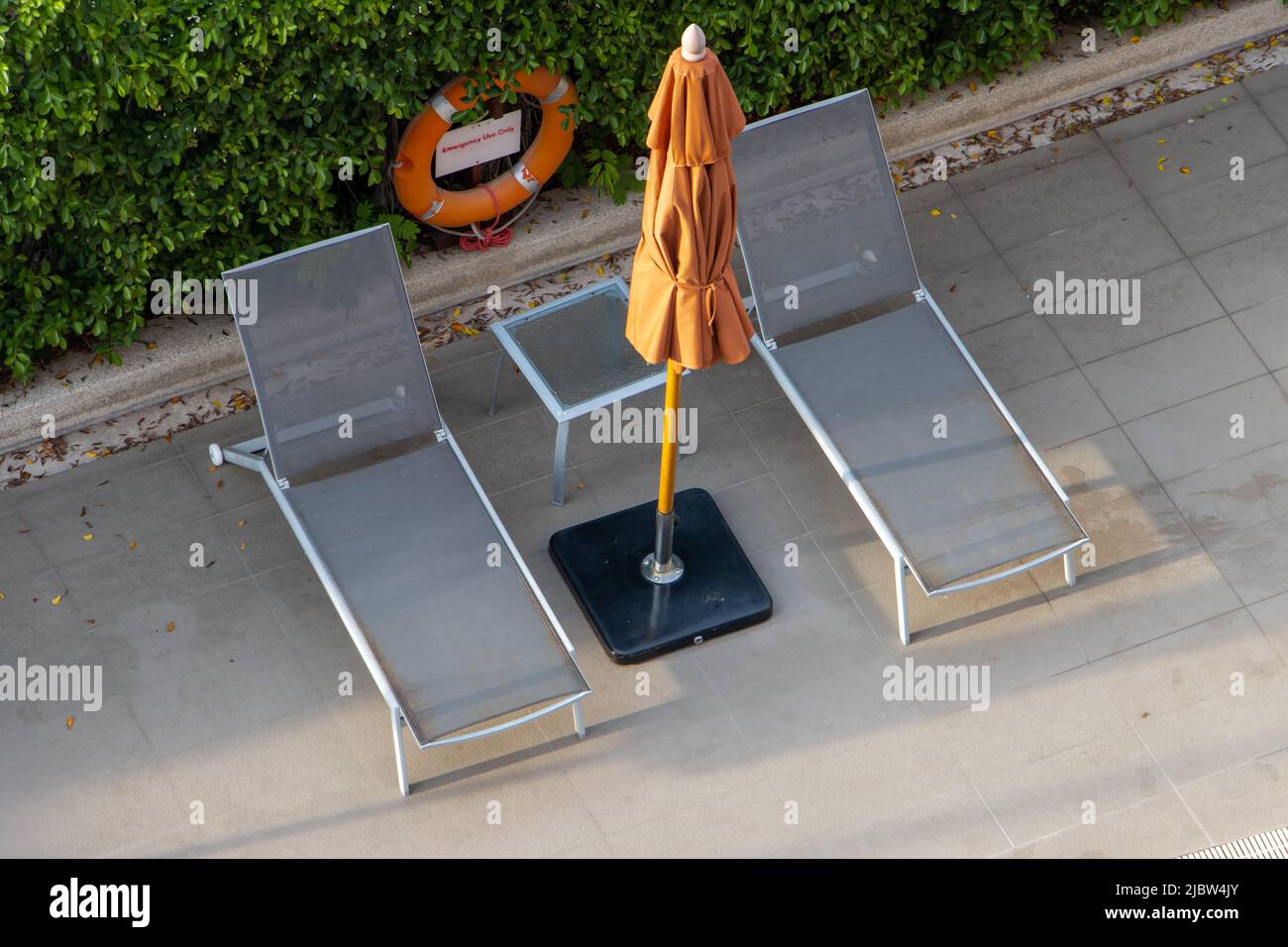 Leerer Liegestuhl mit geschlossenem Sonnenschirm im Resort bei Sonnenuntergang. Stockfoto