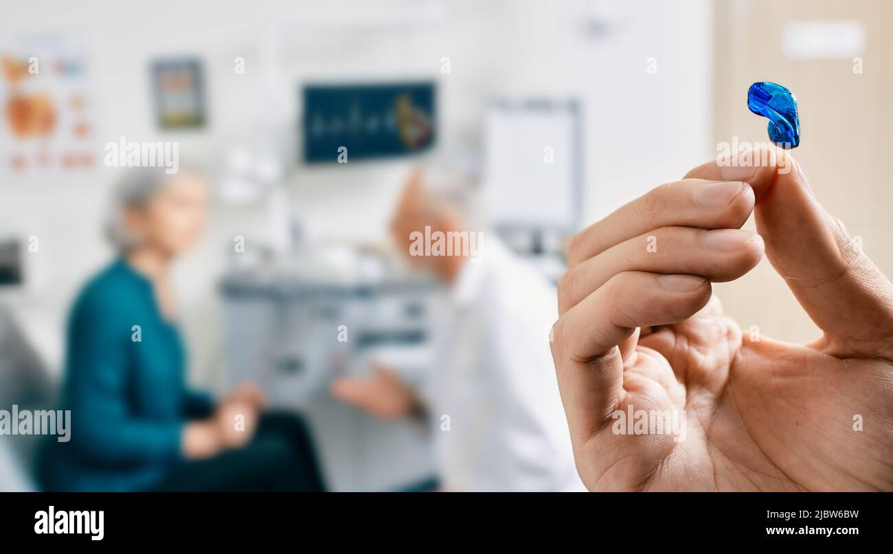 Intra-Ohr-Hörgerät in den Händen des Arztes, Nahaufnahme. Auswahl von Hörgeräten für ältere weibliche Patienten mit Audiologe über dem Hintergrund, weicher Fokus Stockfoto