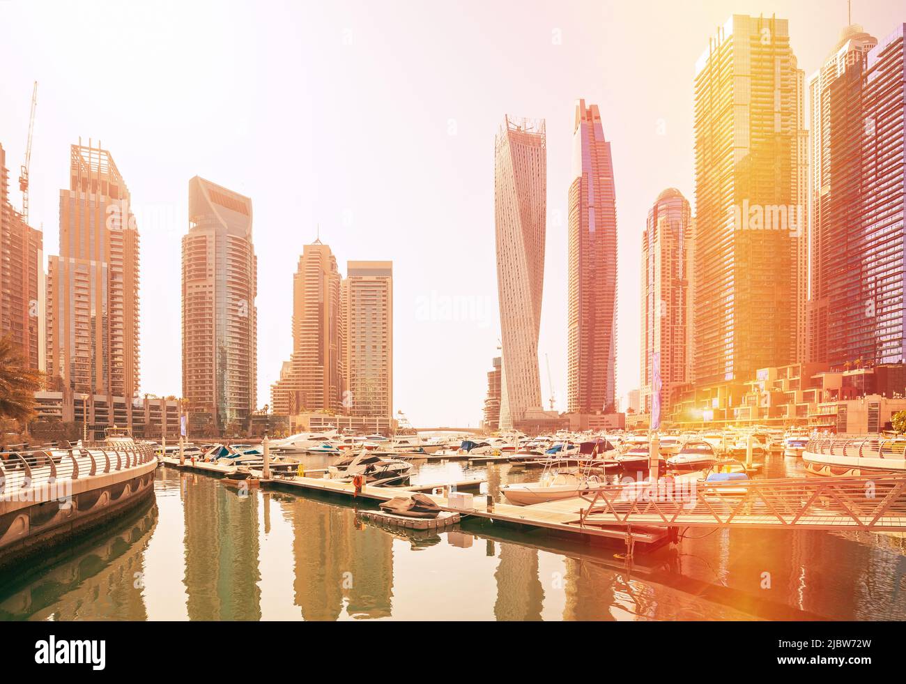 Blick auf die Hochhäuser des Wohnviertels in Dubai Marina und Yachten, die an sonnigen Tagen in der Nähe des Piers festgemacht sind. Dubai Marina Towers. Fackel Sonne, Film Stockfoto