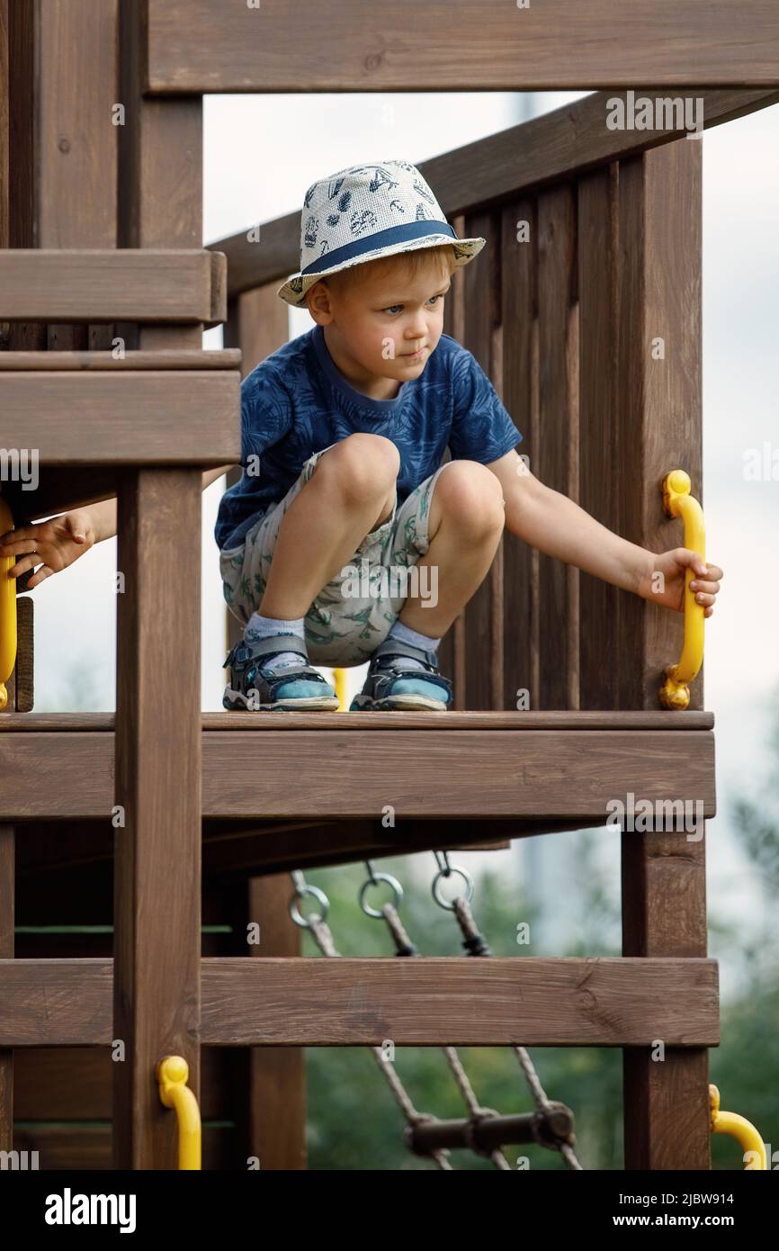 Ein kleiner Junge in einem weißen Hut oben auf einem Holzlot beobachtet die Umgebung Stockfoto