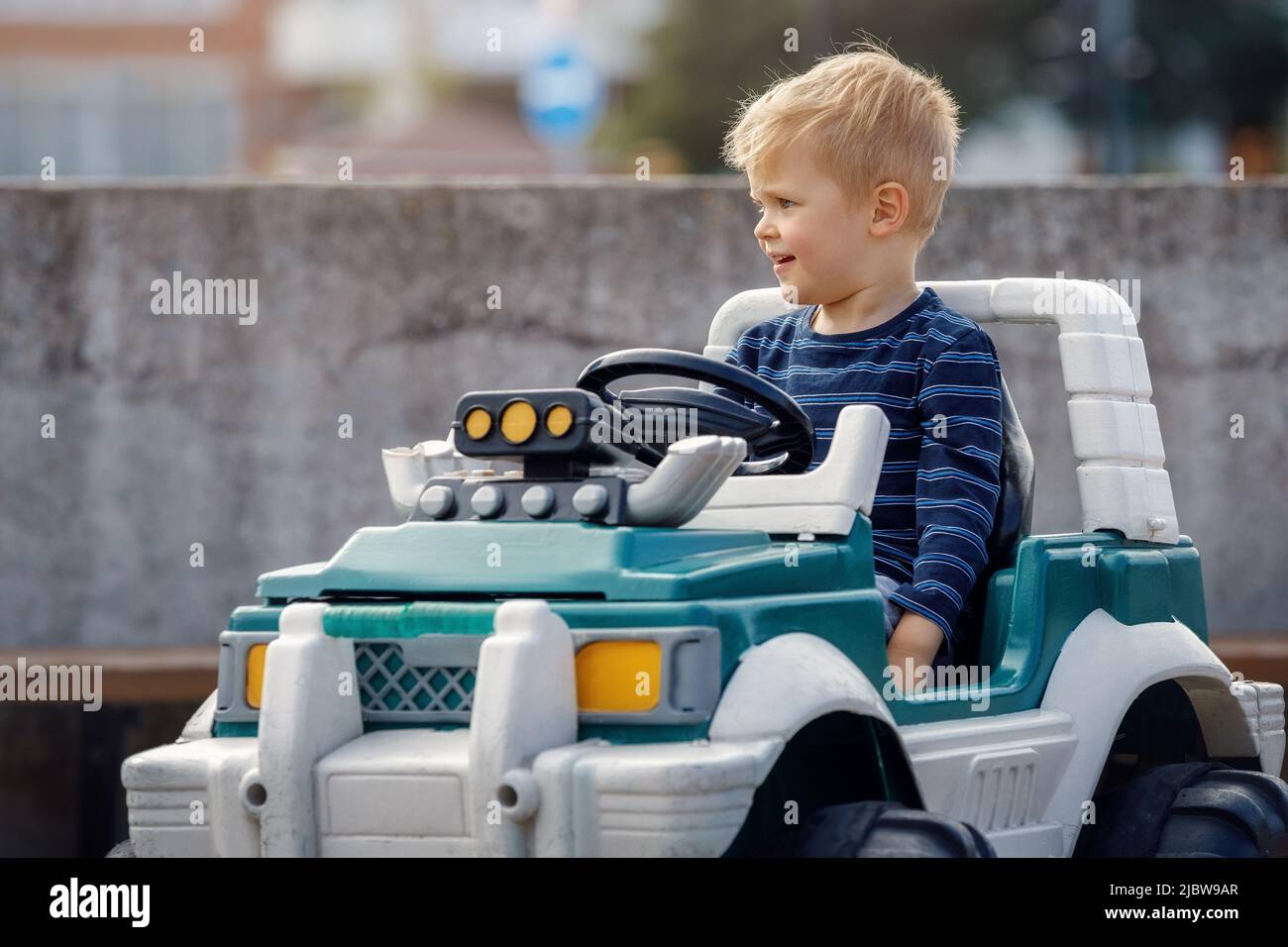 Happy blonde kleinen Jungen in einem großen Spielzeug batteriebetriebenen Auto im Freien. Stockfoto