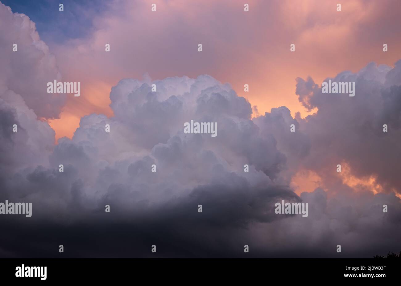 Dramatische und detaillierte Kumuluswolken türmten sich auf einem blauen Himmel zusammen, wobei goldenes und oranges Licht von der Sonne durchschimmert Stockfoto