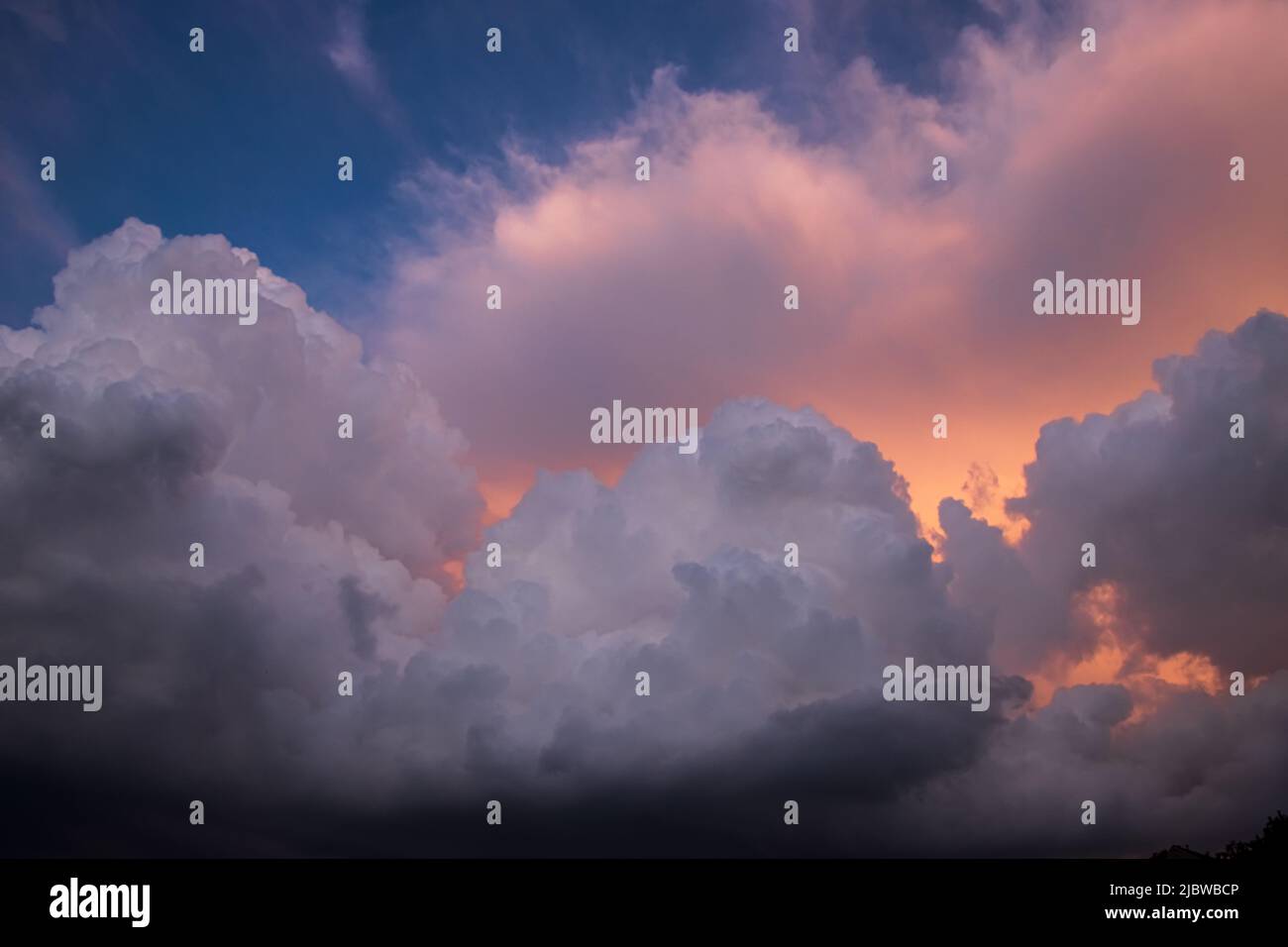 Dramatische und detaillierte Kumuluswolken türmten sich auf einem blauen Himmel zusammen, wobei goldenes und oranges Licht von der Sonne durchschimmert Stockfoto