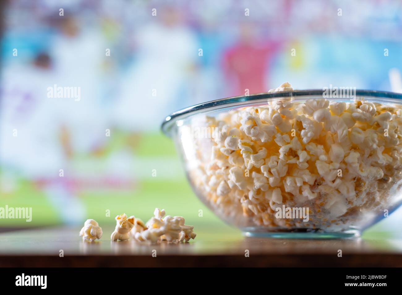 Makroaufnahme. Popcorn in einer großen Glasschüssel auf sportlichem Hintergrund. Ruhe, Entspannung, Tag frei. Sehen Sie sich Ihre Lieblingssportprogramme im Fernsehen an. Es gibt keine p Stockfoto