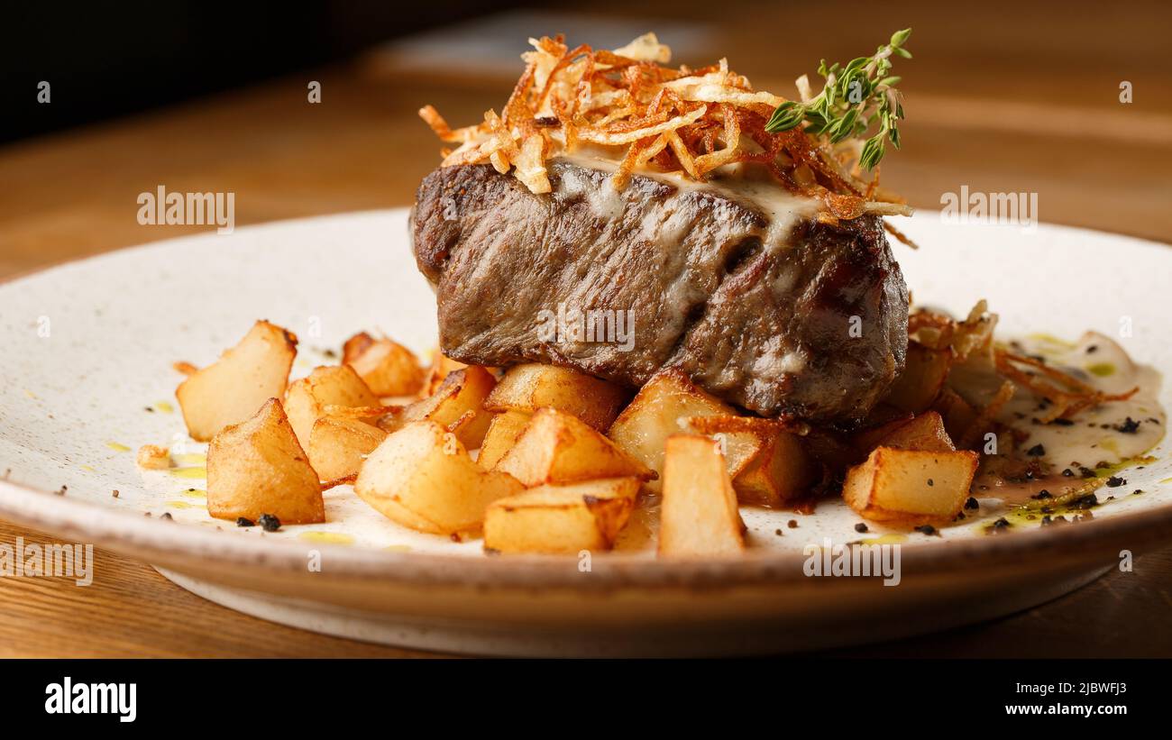 Gegrilltes Steak mit gebackenen goldenen Kartoffeln serviert mit knusprigen Zwiebeln auf einem Backsteingrund. Köstliches Rezept. Schweinefilet gekocht auf Pfanne für Di Stockfoto