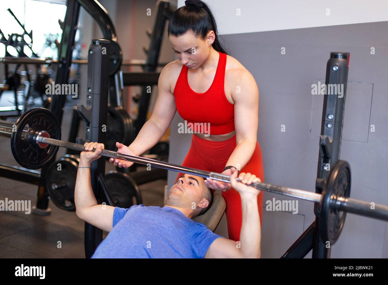 Der junge Personal Trainer hilft beim Training mit Bankdrücken Stockfoto