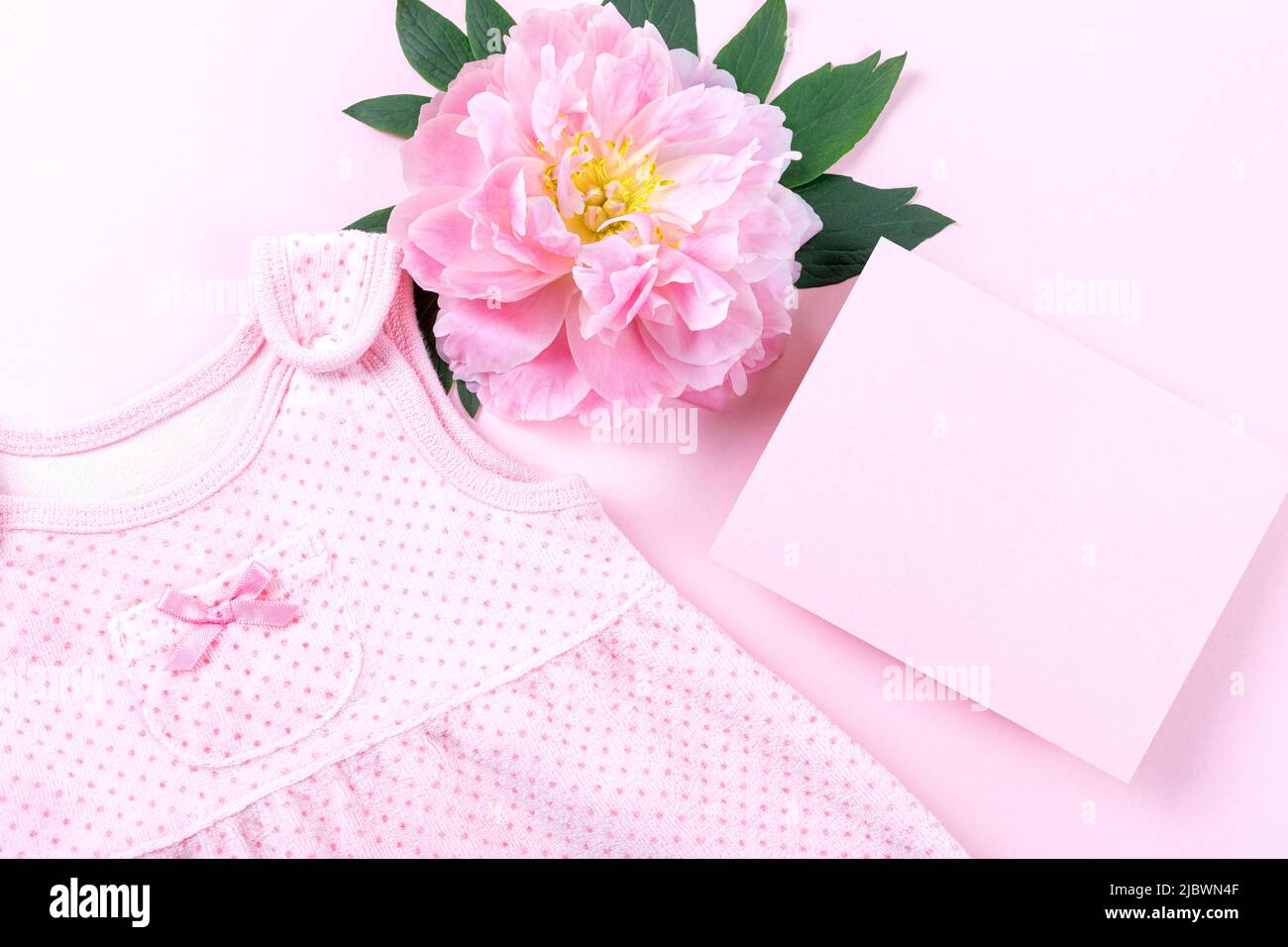 Rosa Baby Mädchen Kleidung und Pfingstrose Blume auf rosa Hintergrund. Babygeburtstag, Einladung oder Grußkarte. Speicherplatz kopieren. Flach liegend. Stockfoto