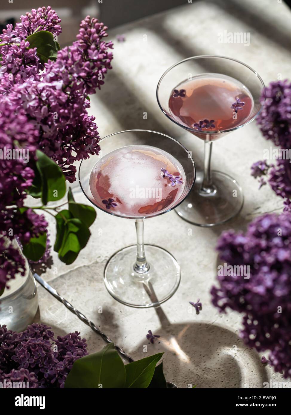 Zwei Roséweingläser mit Fliederblumen und Schatten auf grauem Hintergrund. Sommerdrink für Party, Weinladen, Menü oder Verkostungskonzept Stockfoto