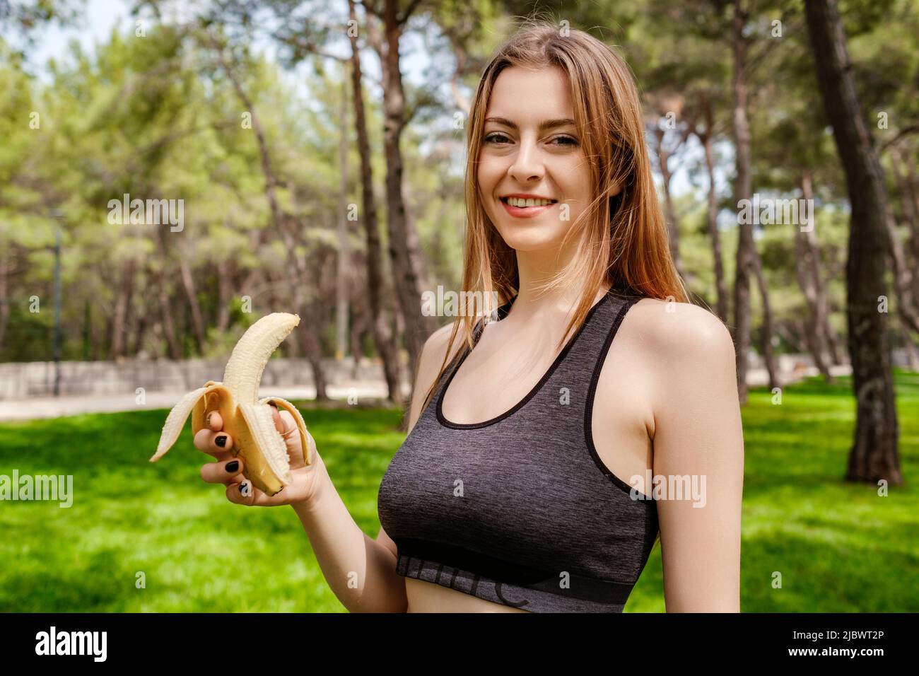 Junge schöne Frau trägt sportliche Kleidung im Stadtpark, essen im Freien gesunde Banane für Kraft und Energie. Outdoor-Sport und gesunde Ernährung a Stockfoto