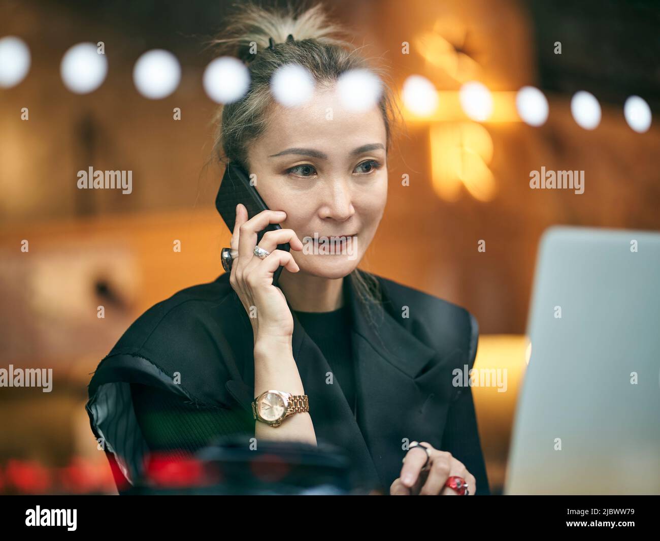 Reife asiatische Geschäftsfrau, die im Café mit Handy und Laptop-Computer arbeitet Stockfoto