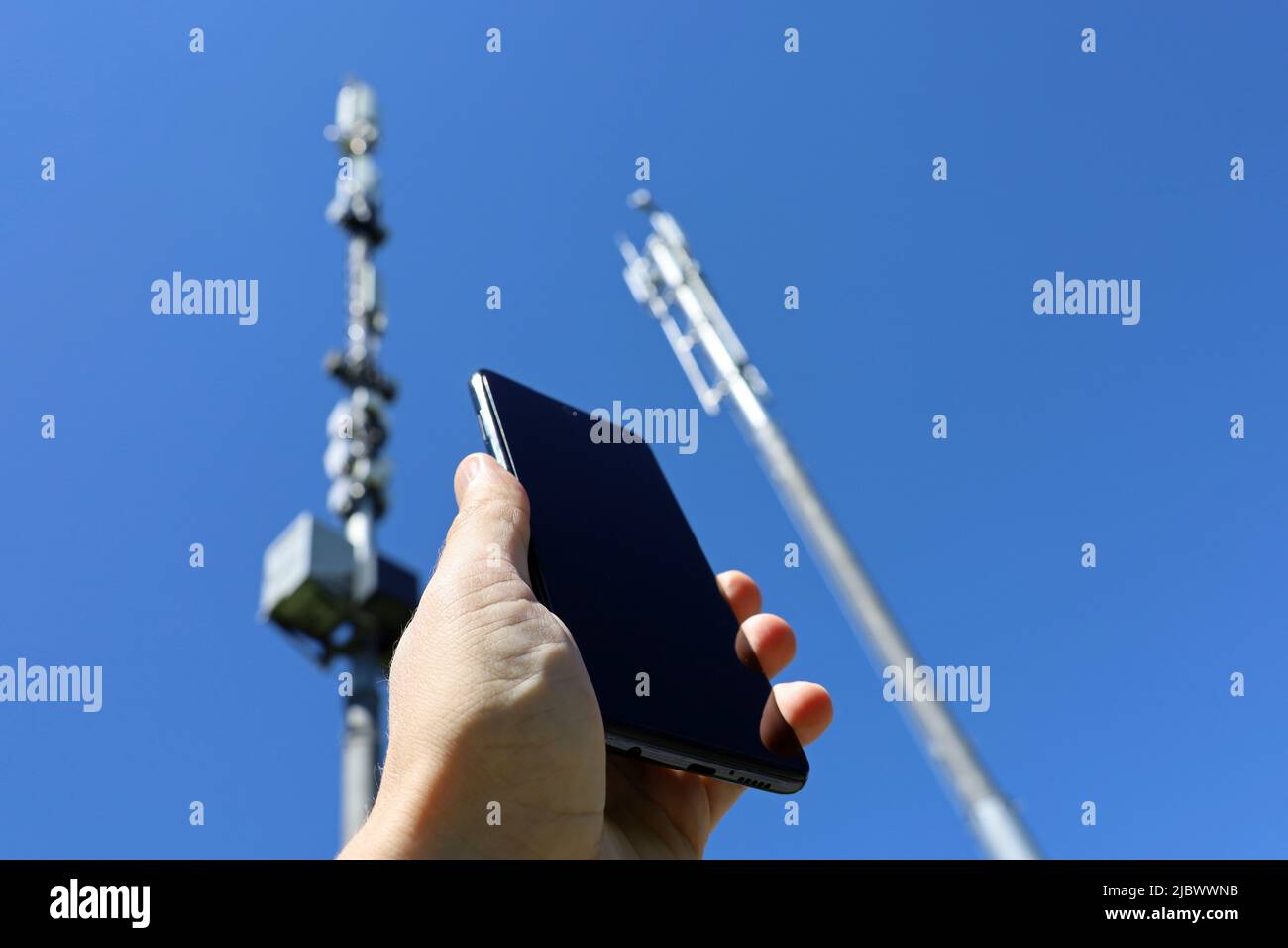 Männliche Hand mit Smartphone auf dem Hintergrund von Zelltürmen. Mobilkommunikationsgeräte, Signalstärke des Telefons Stockfoto