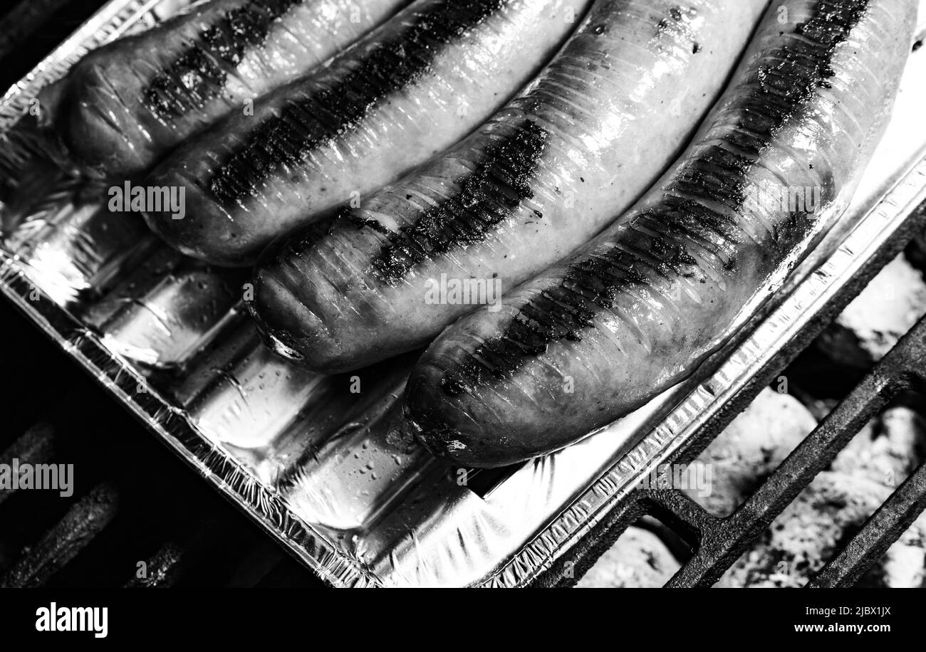 Gegrillte Wurst auf einem Aluminiumkissen. Grill, Zubereitung von Speisen, Backen. Nahaufnahme einer gespülten und leicht gerösteten Wurst auf dem Grill. Stockfoto