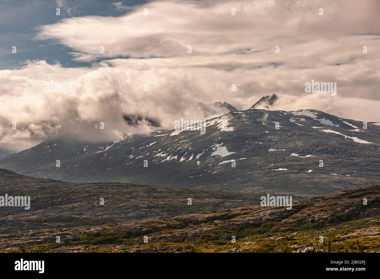 Skagway, Alaska, USA - 20. Juli 2011: Klondike Highway nach Kanada. Die dicke Wolkenlandschaft dringt in die kanadischen Rockies ein, mit Schneepatches hinter trockenem Hochgebirge Stockfoto